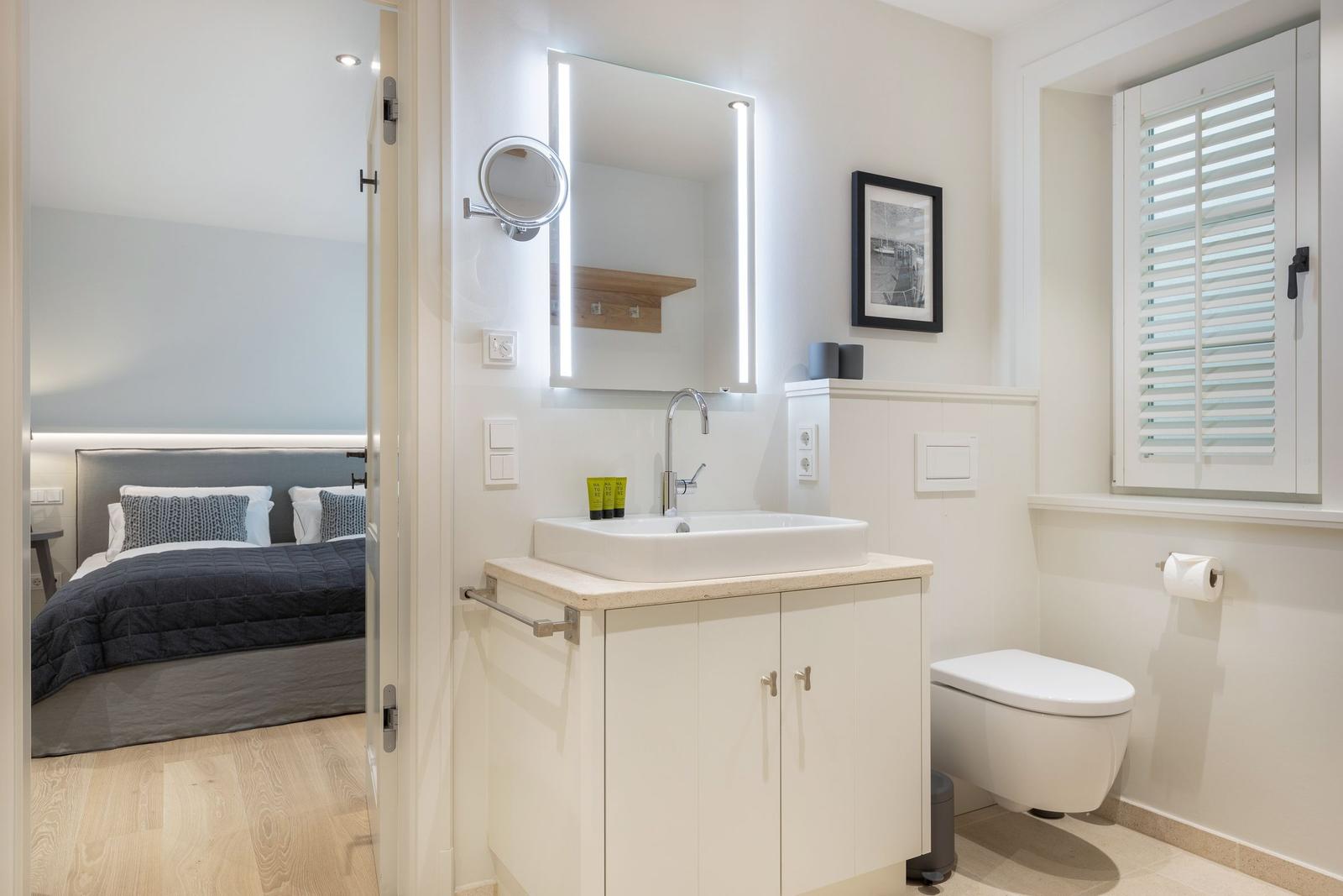 Bathroom with sink, toilet, and mirror. Bedroom with bed visible.