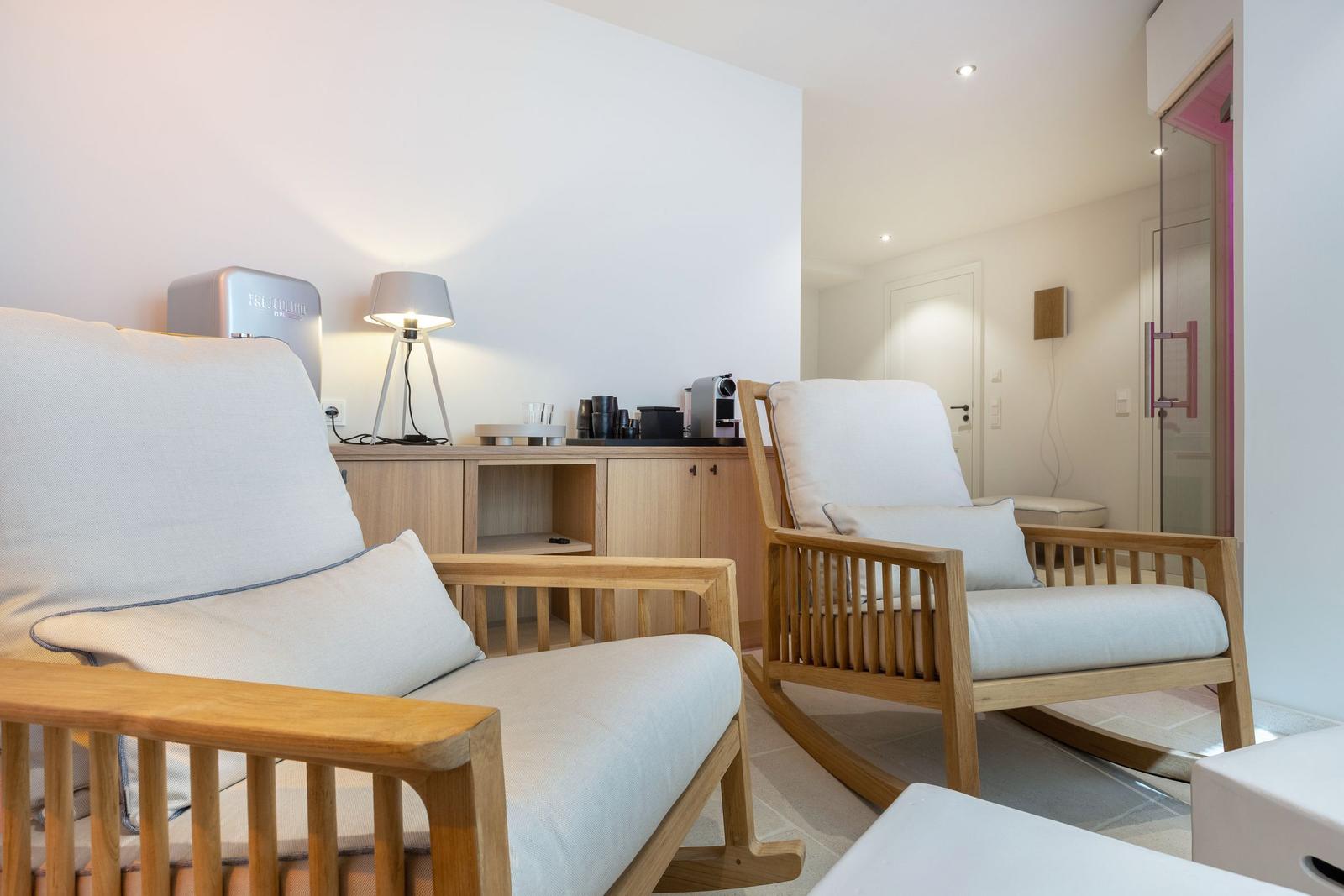Two wooden chairs with light cushions are in a room with a cabinet and lamp.