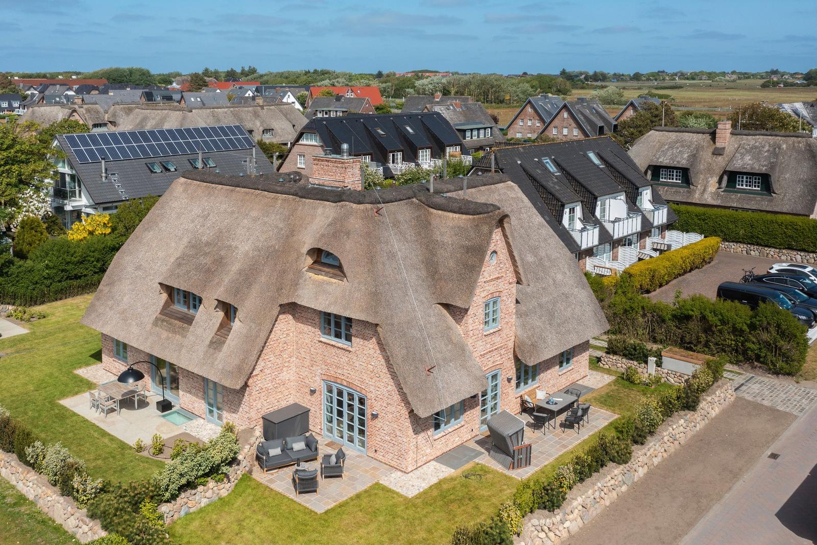 Farmhouse with thatched roof, terrace, and garden. Surrounded by other houses.