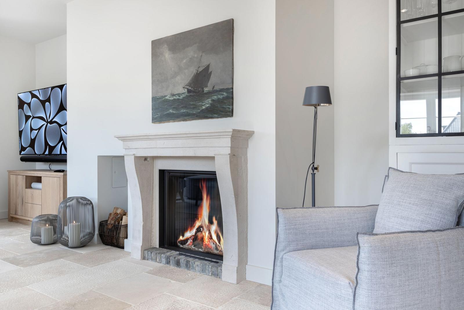 Fireplace with burning fire, gray sofa, and wall painting with sailboat.