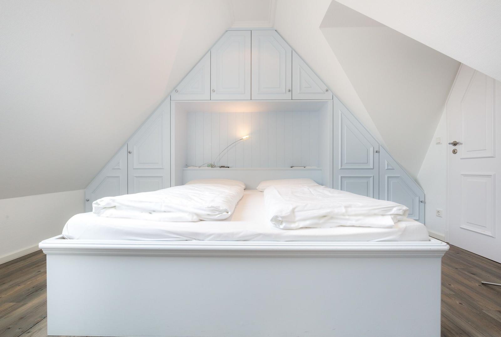 Doppelbett unter Dachschräge mit integrierten Schränken und Nachttischbeleuchtung.