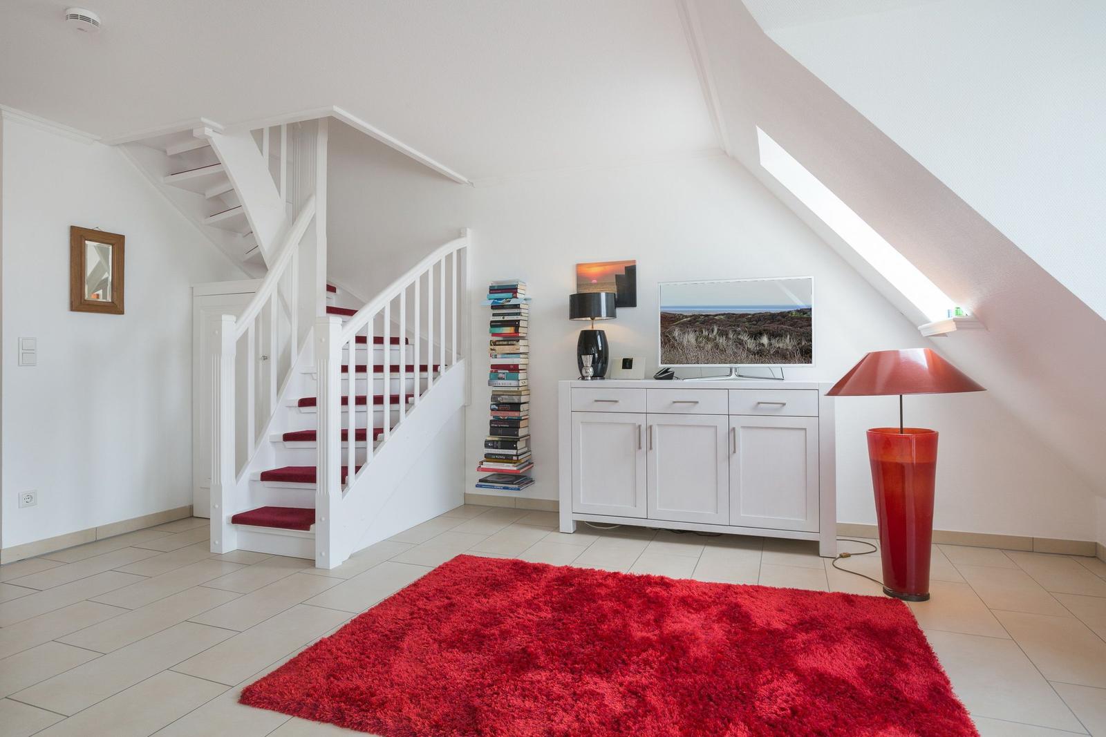 Wohnzimmer mit rotem Teppich, weißer Treppe und Fernseher auf Schrank.