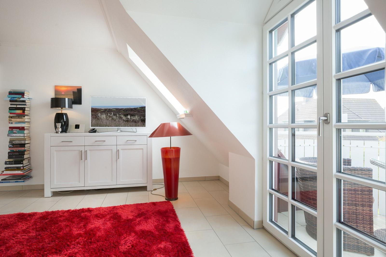 Wohnraum mit rotem Teppich, TV und großem Fenster zur Terrasse.
