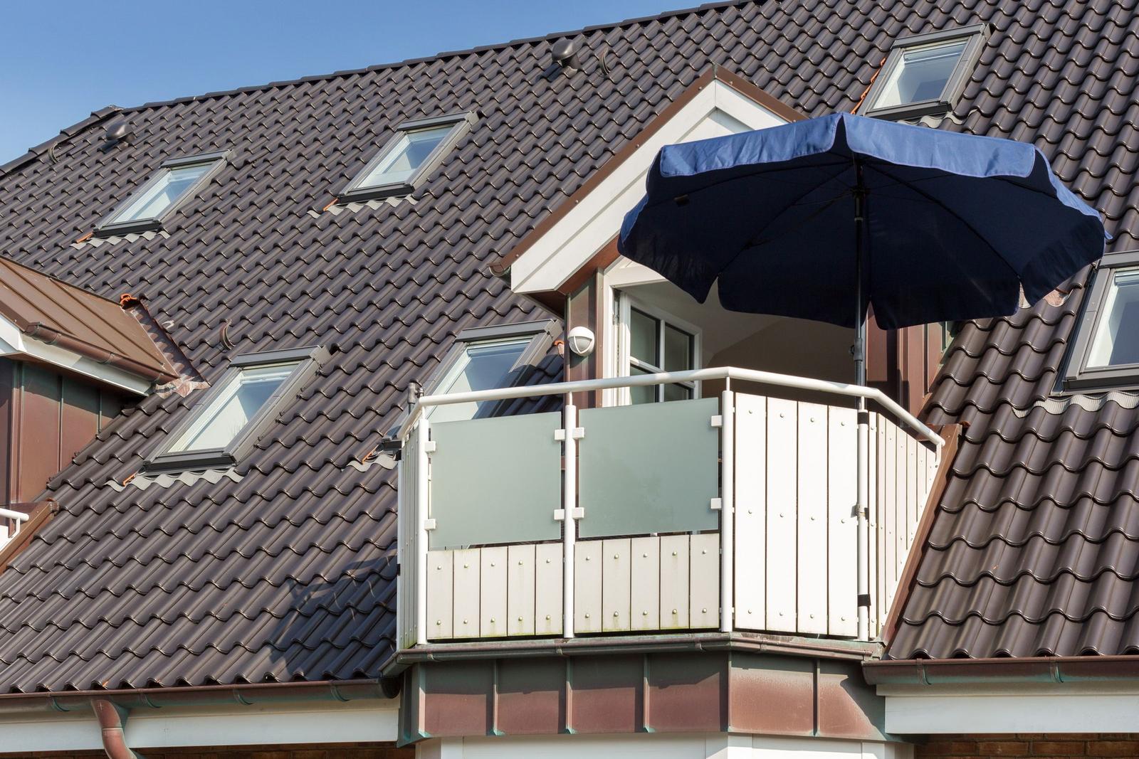 Terrasse mit blauem Sonnenschirm und Glasgeländer an Haus mit Dachfenstern.