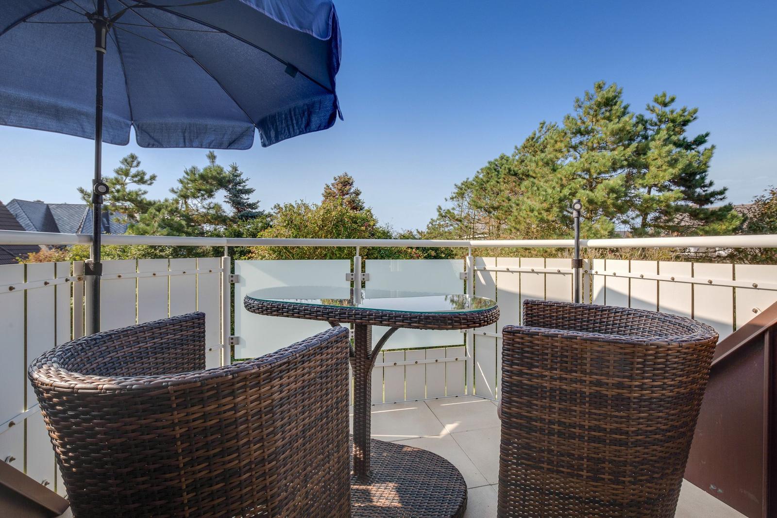 Terrasse mit Tisch, Stühlen und Sonnenschirm. Blick auf Bäume und Himmel.