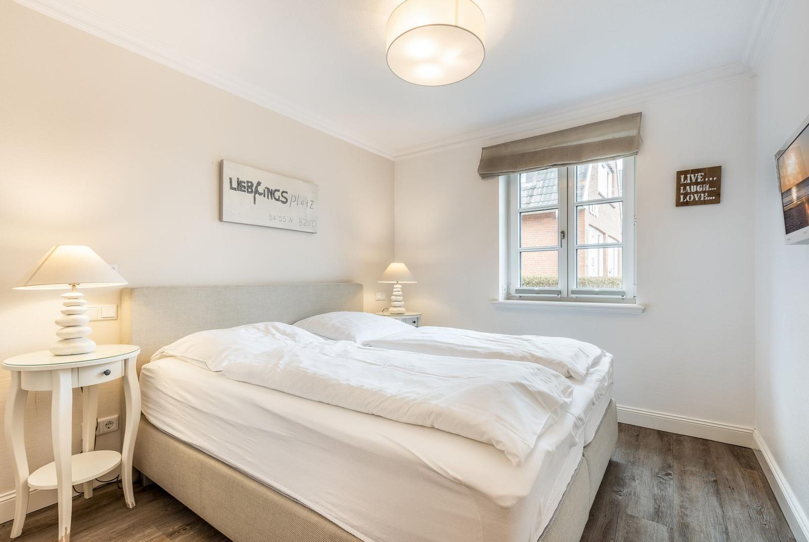 Bedroom with double bed, two nightstands, and window overlooking buildings.