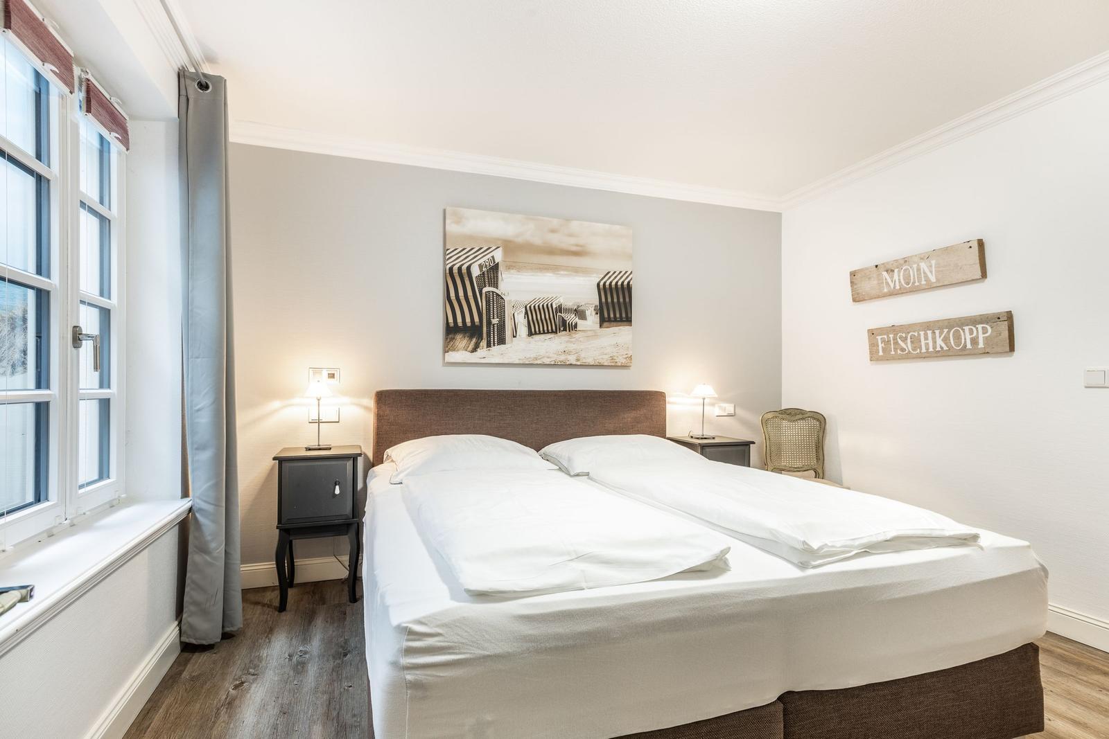 Bedroom with double bed, window, and wall art. Two nightstands with lamps.