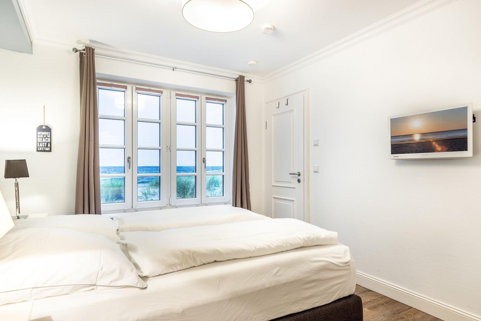 Bedroom with sea view, white bed, windows, and wall picture.