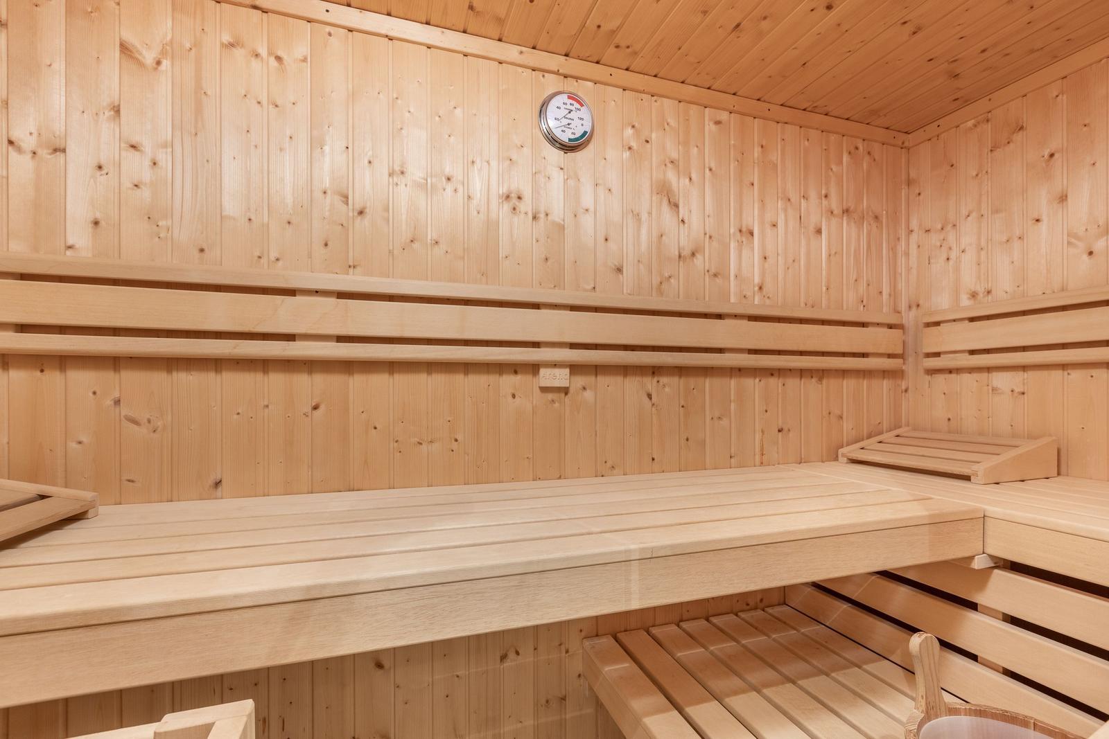 Sauna with wooden benches and temperature gauge on the wall.