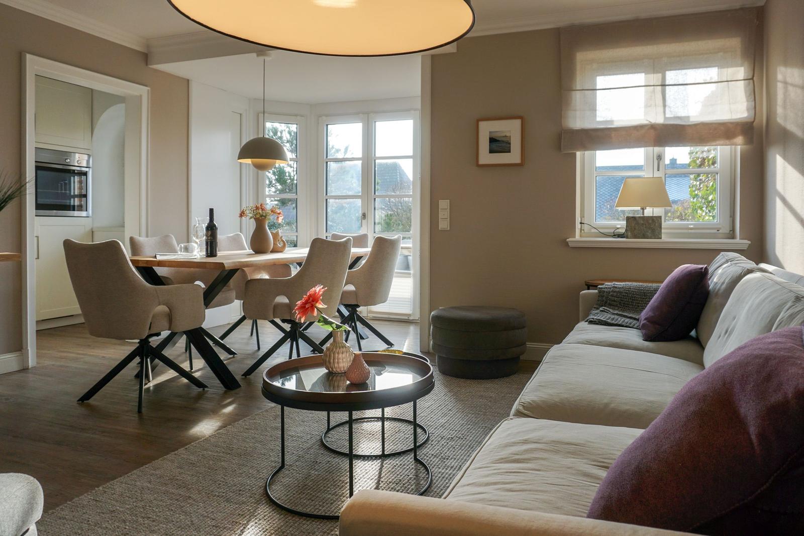 Living and dining area with sofa, table, and chairs. Kitchen in the background.