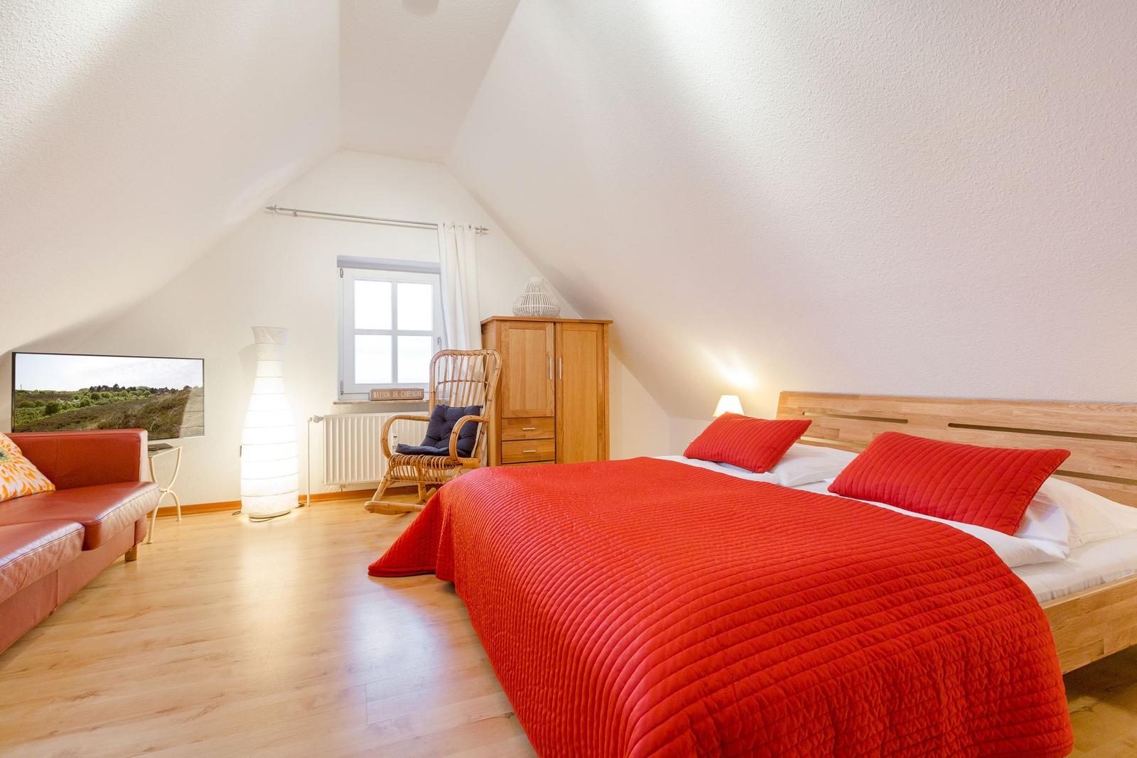 Schlafzimmer mit rotem Bett, Holzboden und Dachschrägen