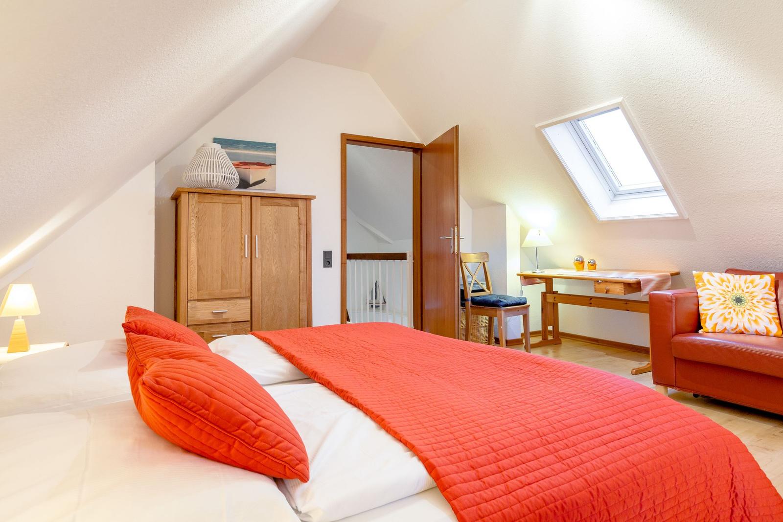 Schlafzimmer mit Dachschrägen, Bett, Schrank, Schreibtisch und Sofa.