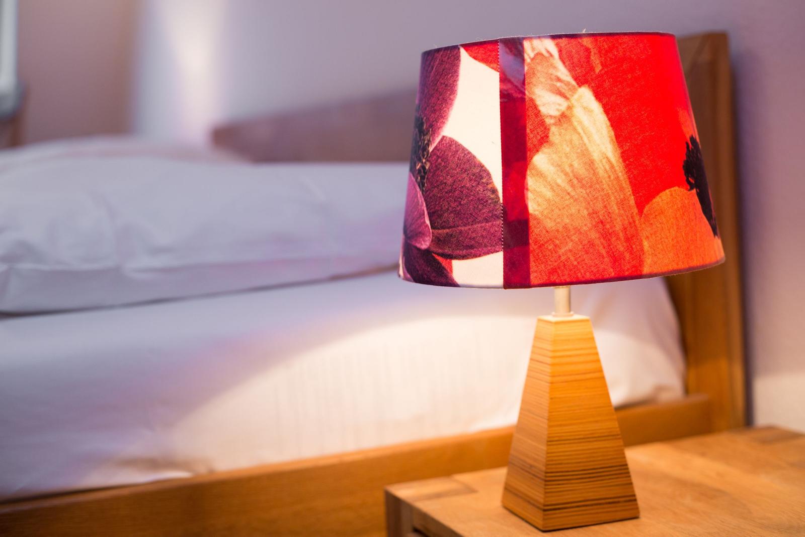 Tischlampe mit farbigem Schirm auf Nachttisch neben Bett