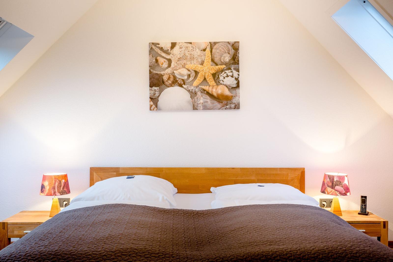Schlafzimmer mit Bett, Nachttischen und Wandbild mit Muscheln und Seestern.
