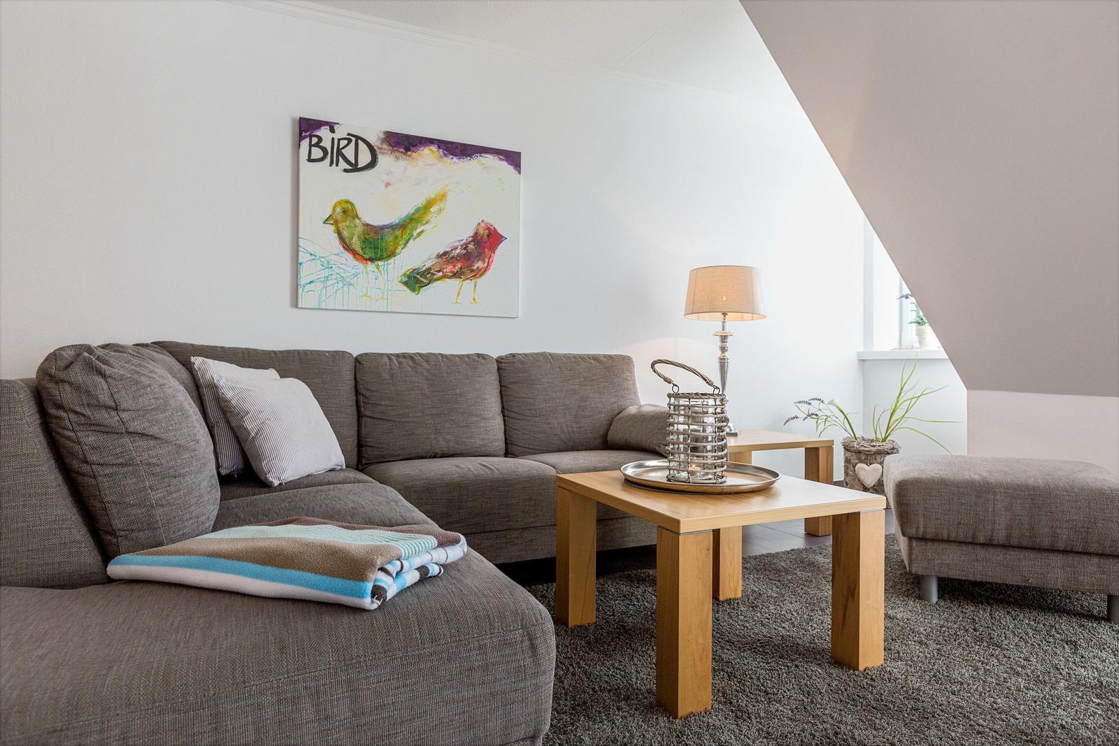 A living room with a gray sofa, wooden table, and wall art with birds.
