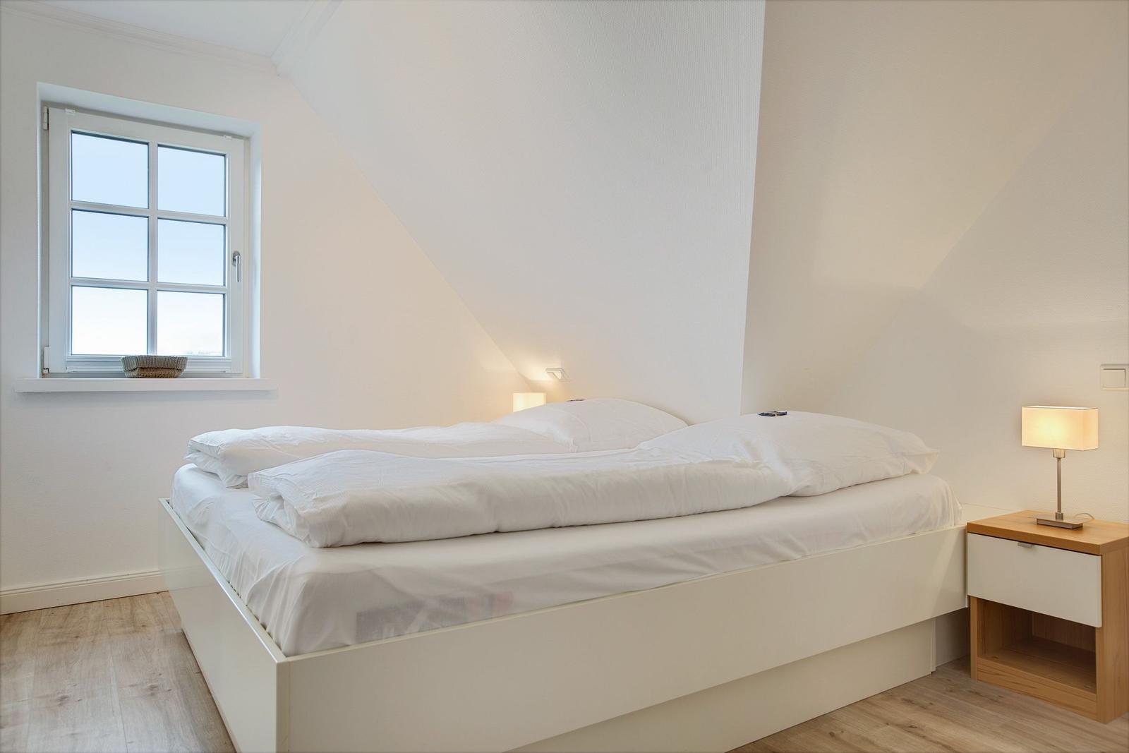 Bedroom with white bed, nightstand, and window.