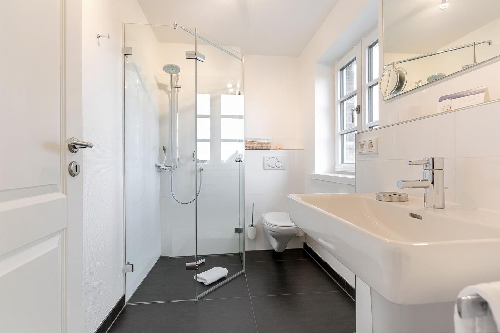 Bathroom with shower, sink, and toilet. Window provides daylight.