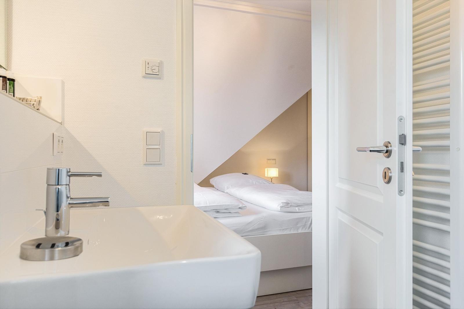 Bathroom with sink and view into bedroom with bed and lamp.