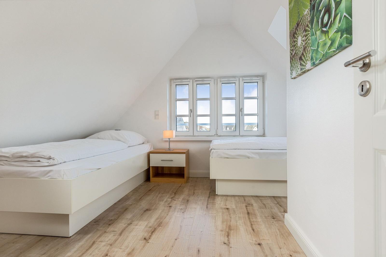 Two single beds with nightstand and window in attic room.