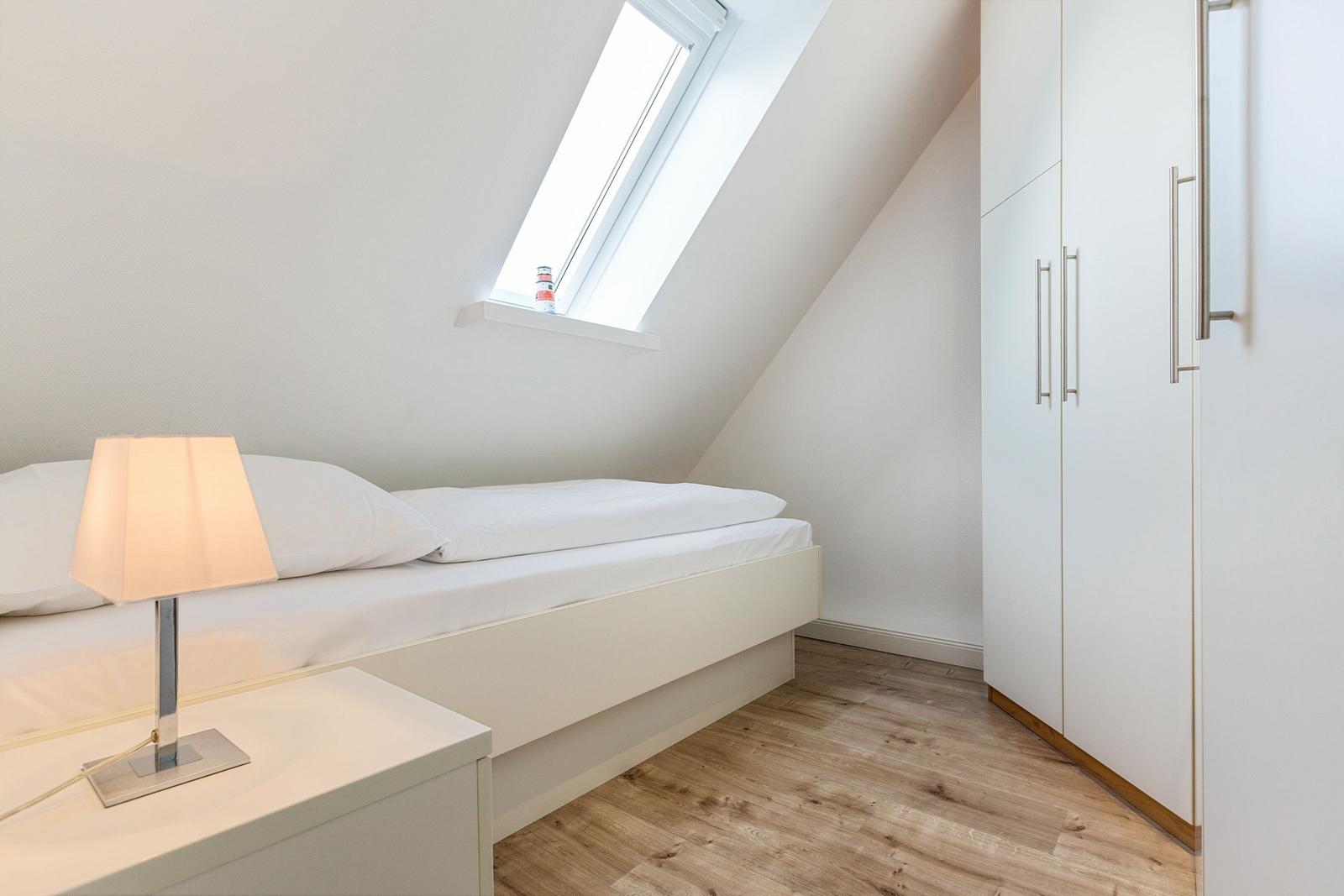 Bedroom with sloped ceiling, bed, nightstand, and wardrobe.