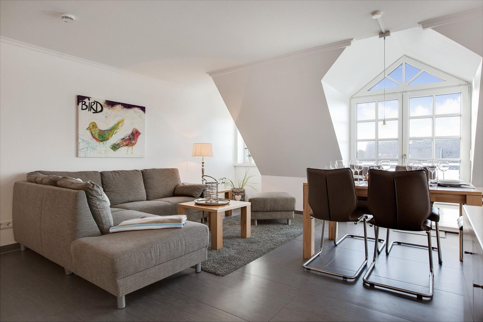 Living and dining area with sofa, table and chairs. Large windows and wall art with birds.