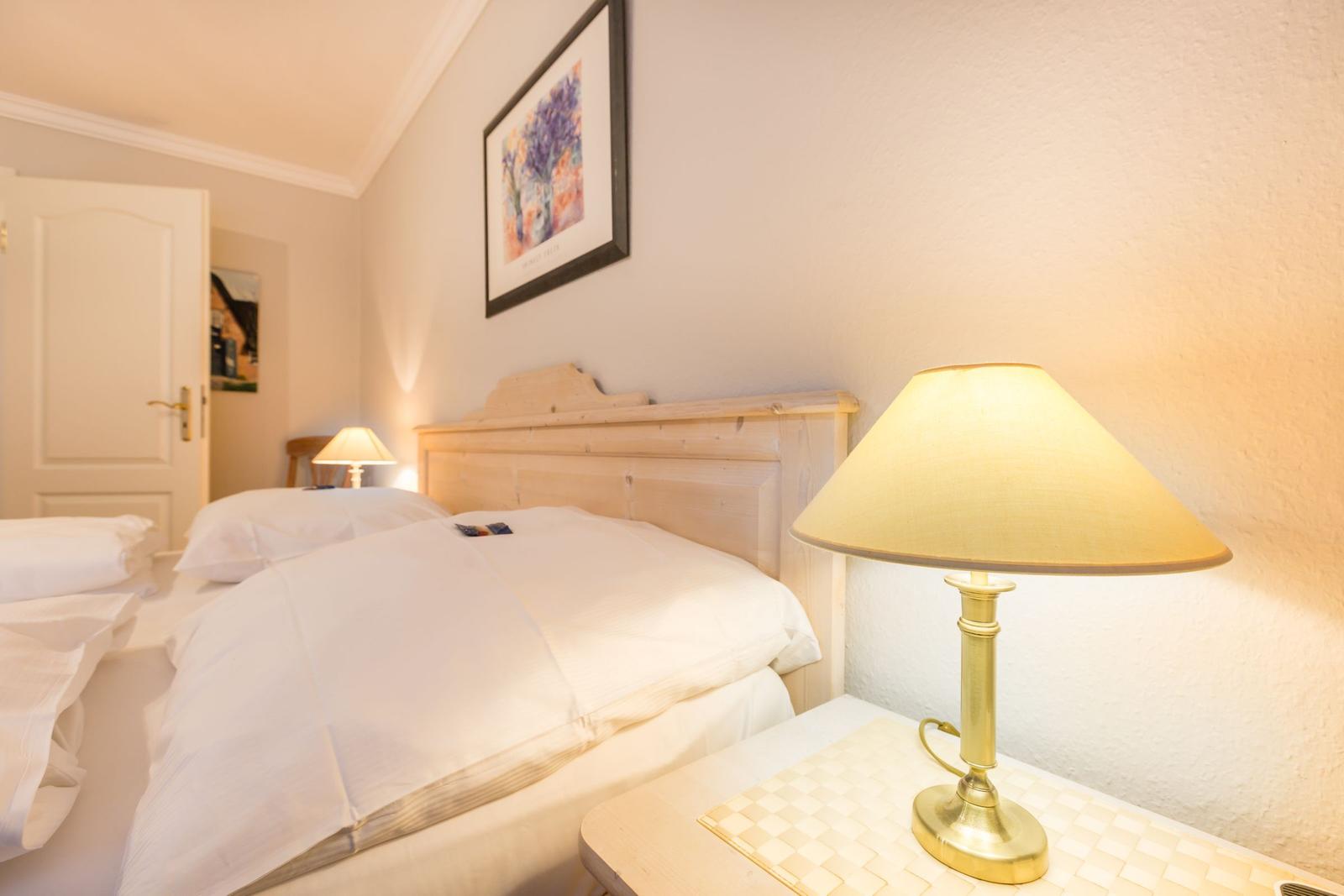 A bed with white linens, nightstand with lamp and wall art.