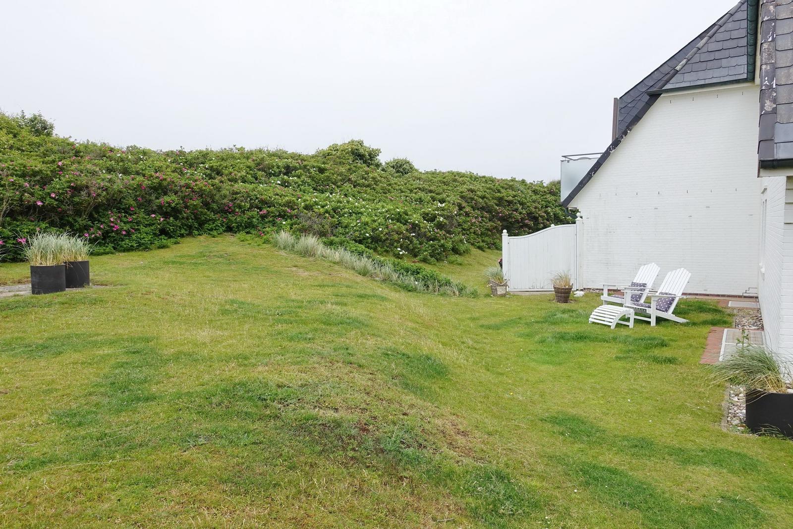 Lawn with grass, white garden furniture, and hedge with flowers.