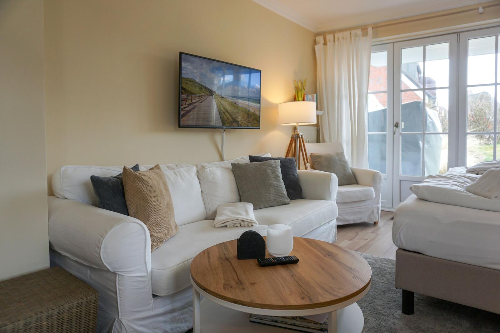 Living area with sofa, TV, and sleeping area. French doors lead outside.