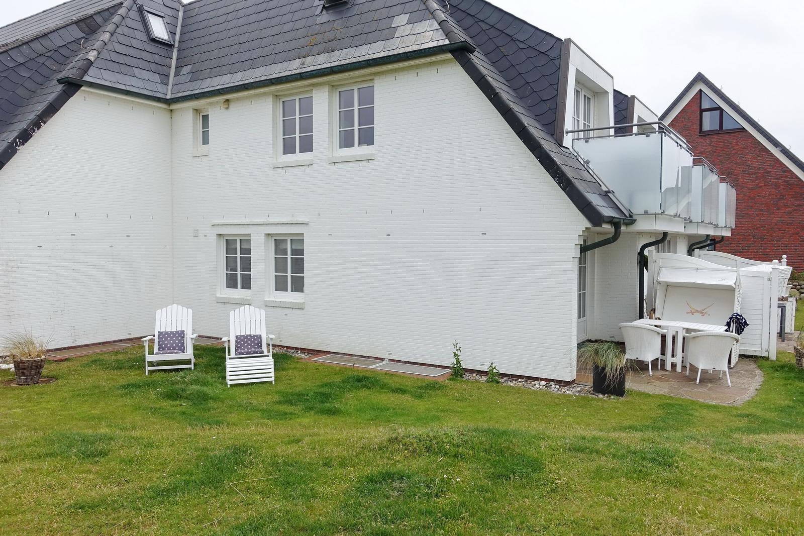 White house with garden, two chairs, and terrace with table.