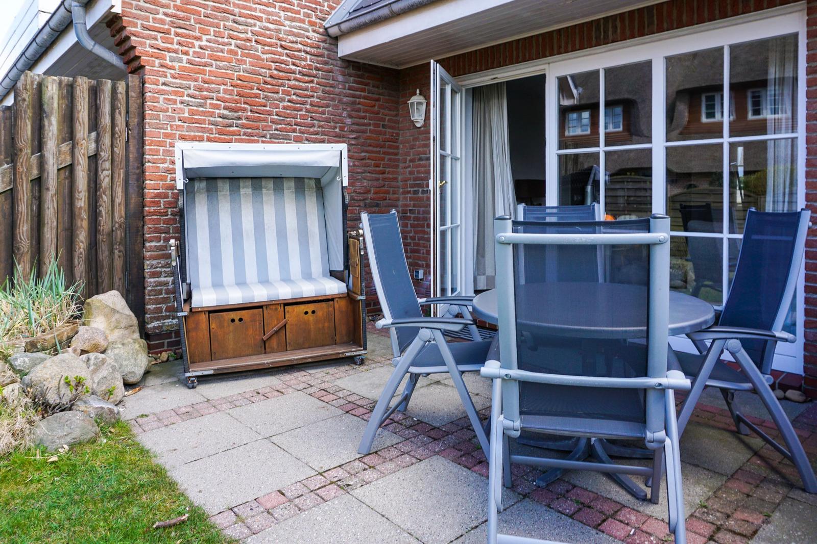 Terrasse mit Strandkorb und Sitzgruppe vor Haus mit Fenster