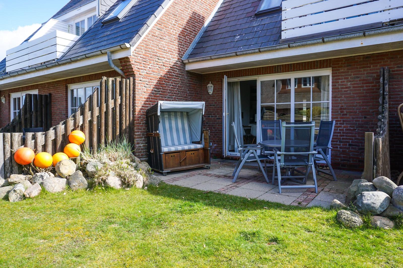 Terrasse mit Sitzgruppe, Strandkorb und Gartenbereich vor einem Backsteinhaus.