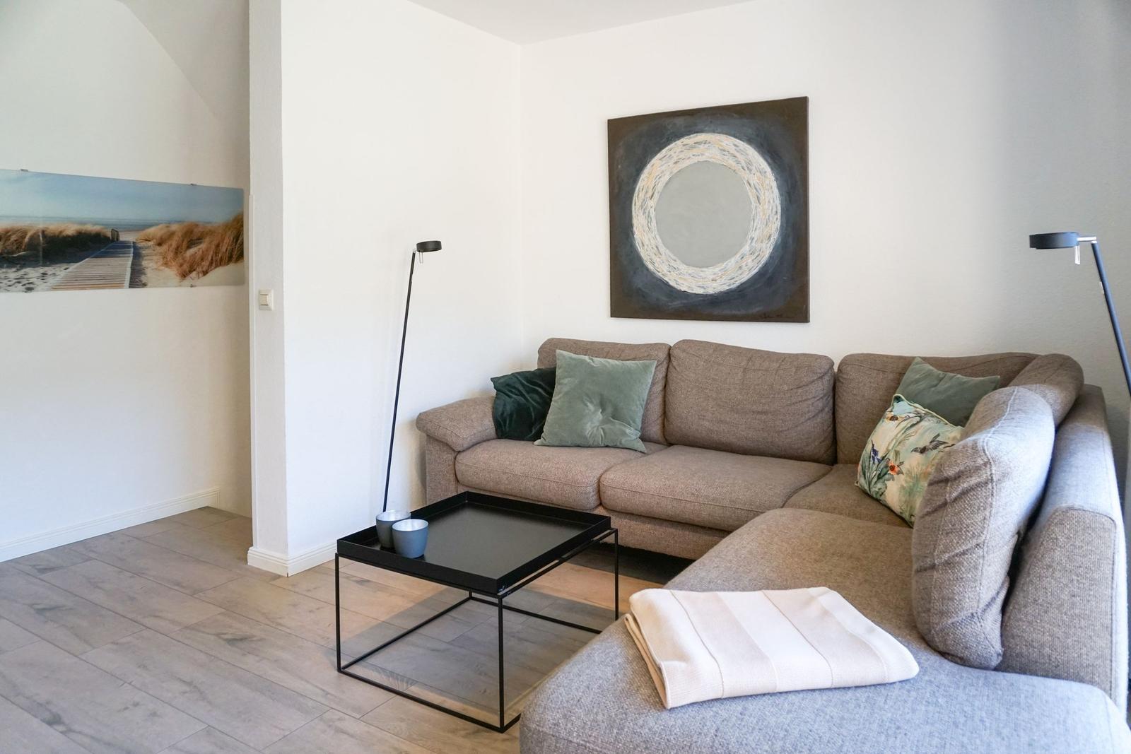 Wohnzimmer mit grauem Sofa, Tisch und Wandbildern.