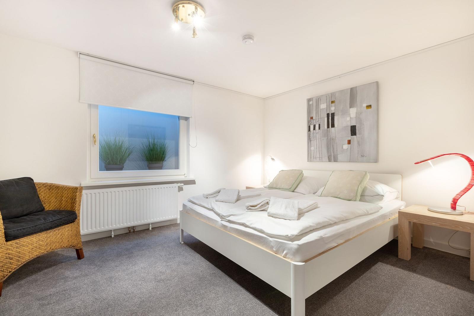 Schlafzimmer mit Bett, Fenster und Sessel.