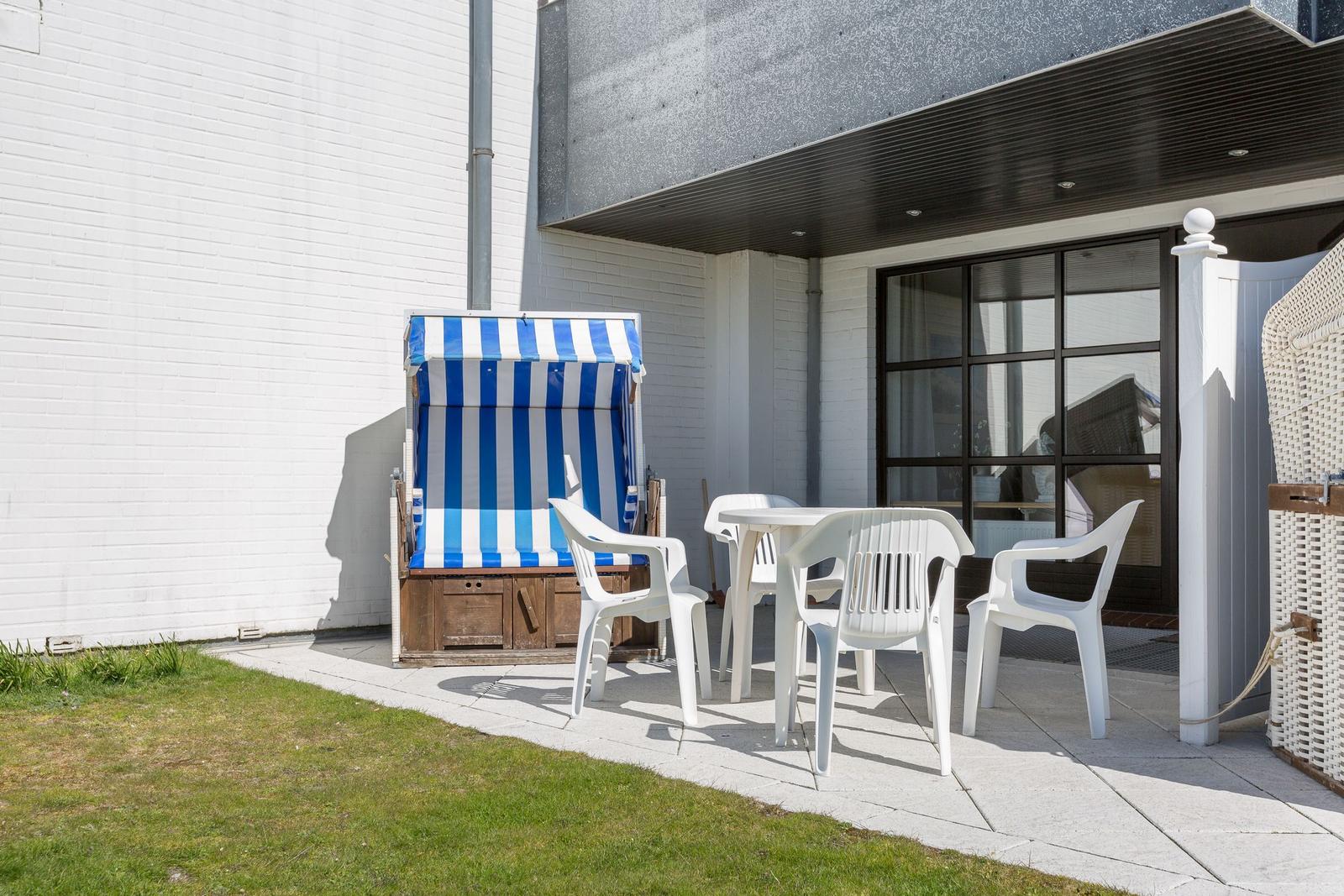 Terrasse mit weißem Tisch, Stühlen und Strandkorb mit blau-weißem Streifen.