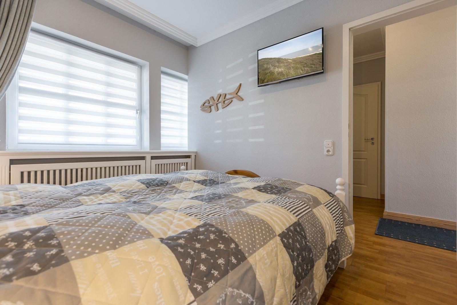 Schlafzimmer mit Bett, TV und Fenstern mit Jalousien.