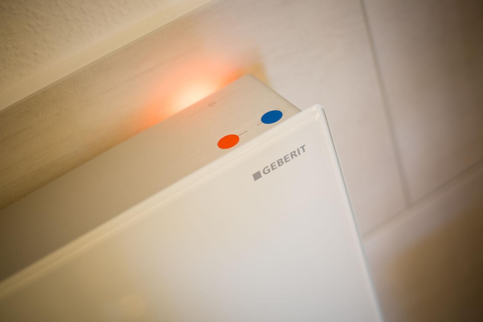 Weiße Toilettenkabine mit orangefarbenem Licht und blau-orangefarbenen Markierungen.