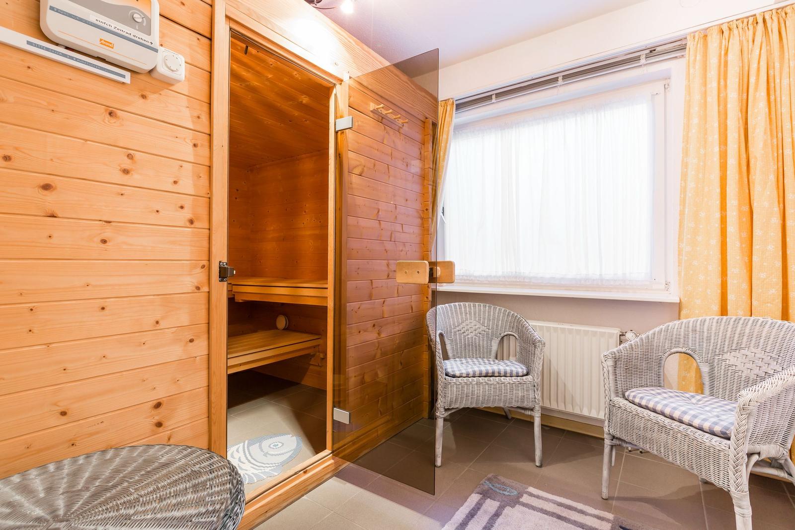 Sauna mit Holzwand, Sitzbänken und zwei Stühlen vor Fenster.