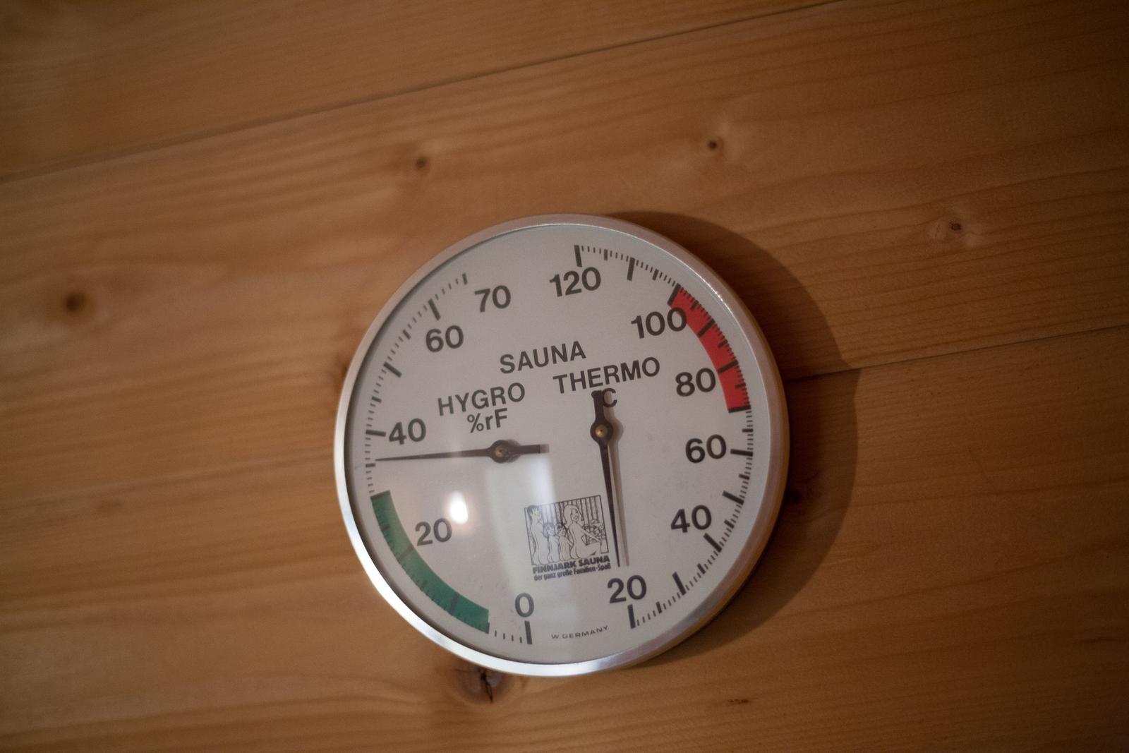 Sauna-Thermometer an Holzwand montiert, zeigt Temperatur und Luftfeuchtigkeit an.