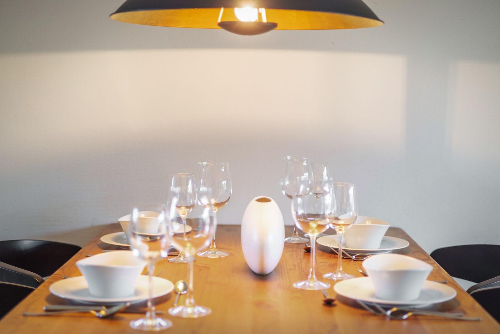 Holztisch mit weißen Tellern, Gläsern und einem weißen Vase unter einer Lampe.