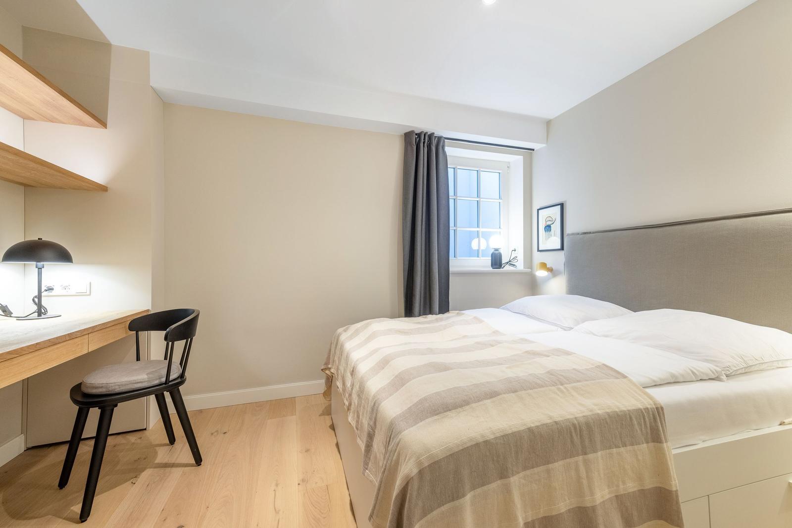 Schlafzimmer mit Bett, Schreibtisch und Fenster.