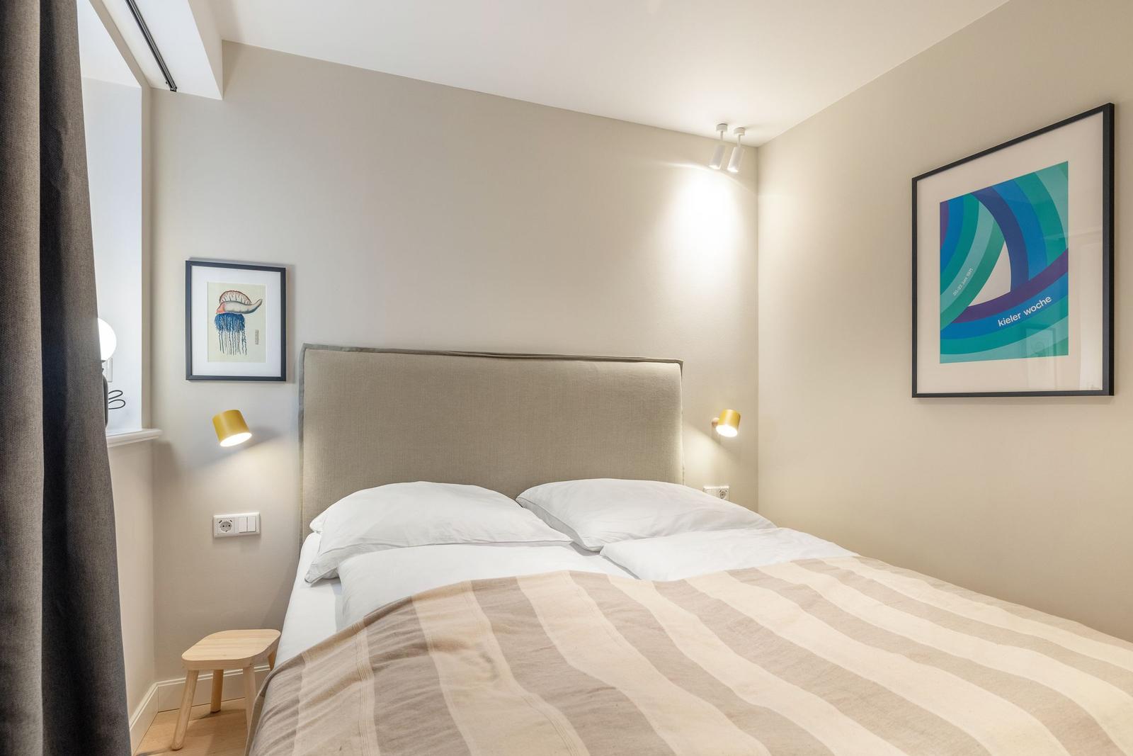 Schlafzimmer mit Doppelbett, Wandlampen und Kunstwerken an den Wänden.