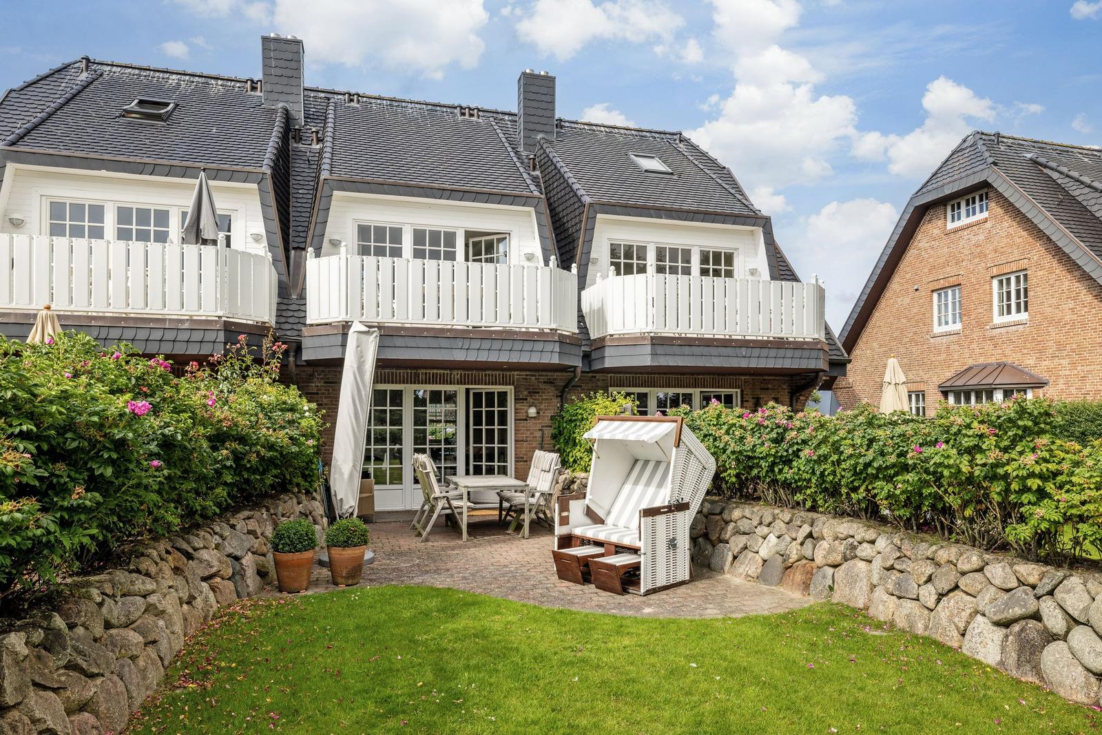 Haus mit Balkonen, Terrasse und Garten. Ein Strandkorb steht auf dem Hof.