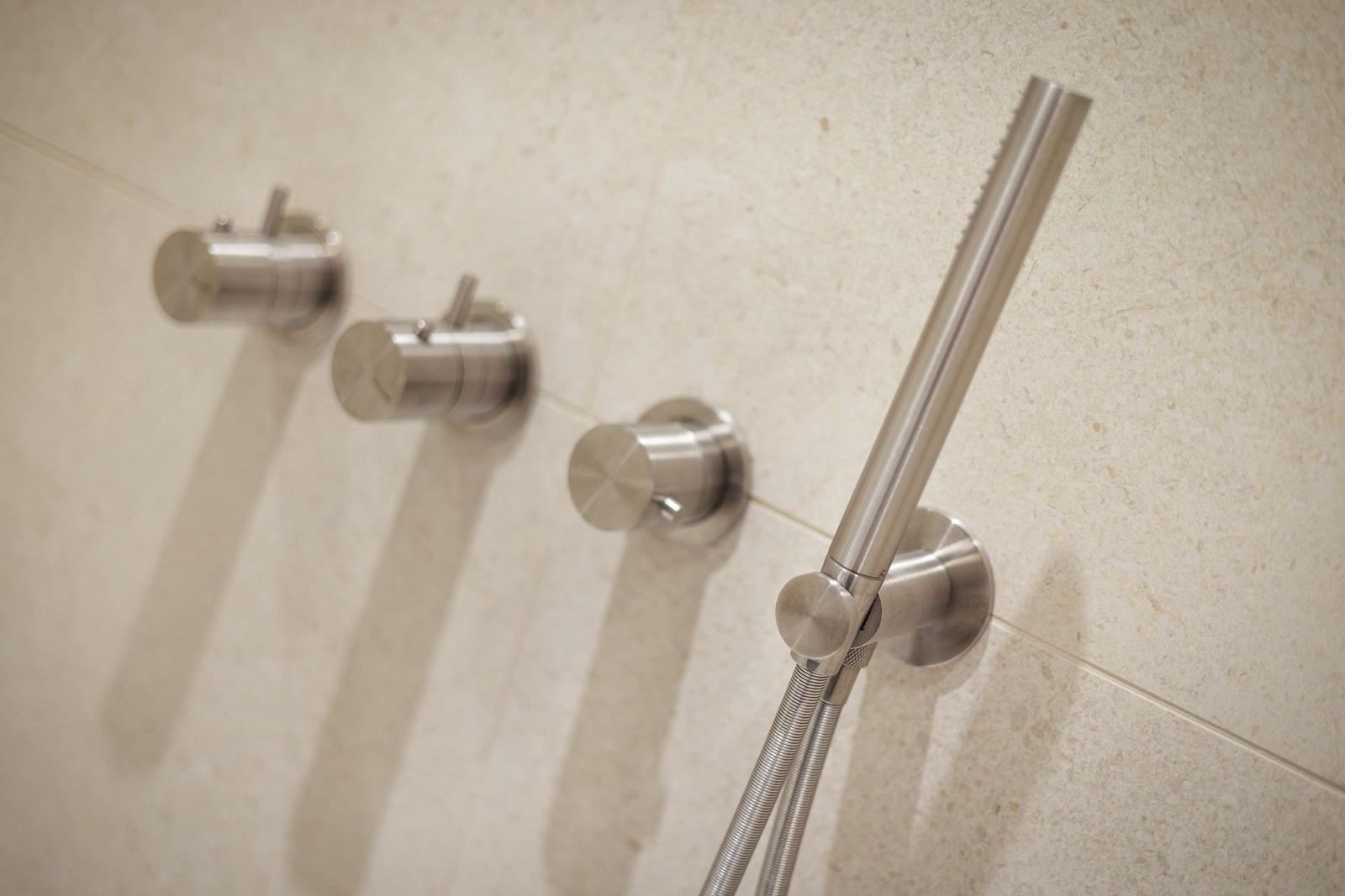 Duschkopf und Bedienelemente an Wand mit Steinfliesen