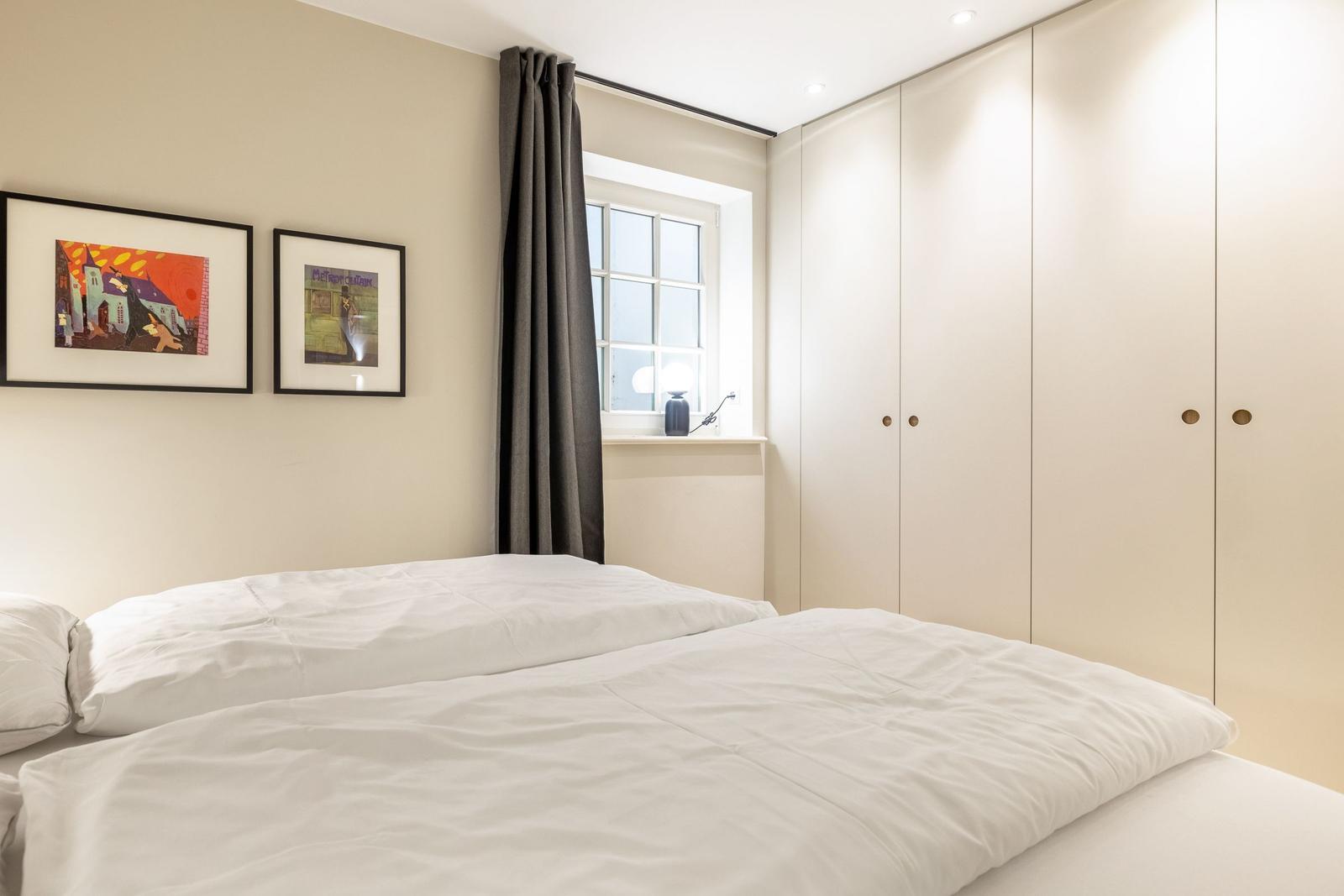 Schlafzimmer mit Bett, Kleiderschrank und Fenster mit Vorhang.
