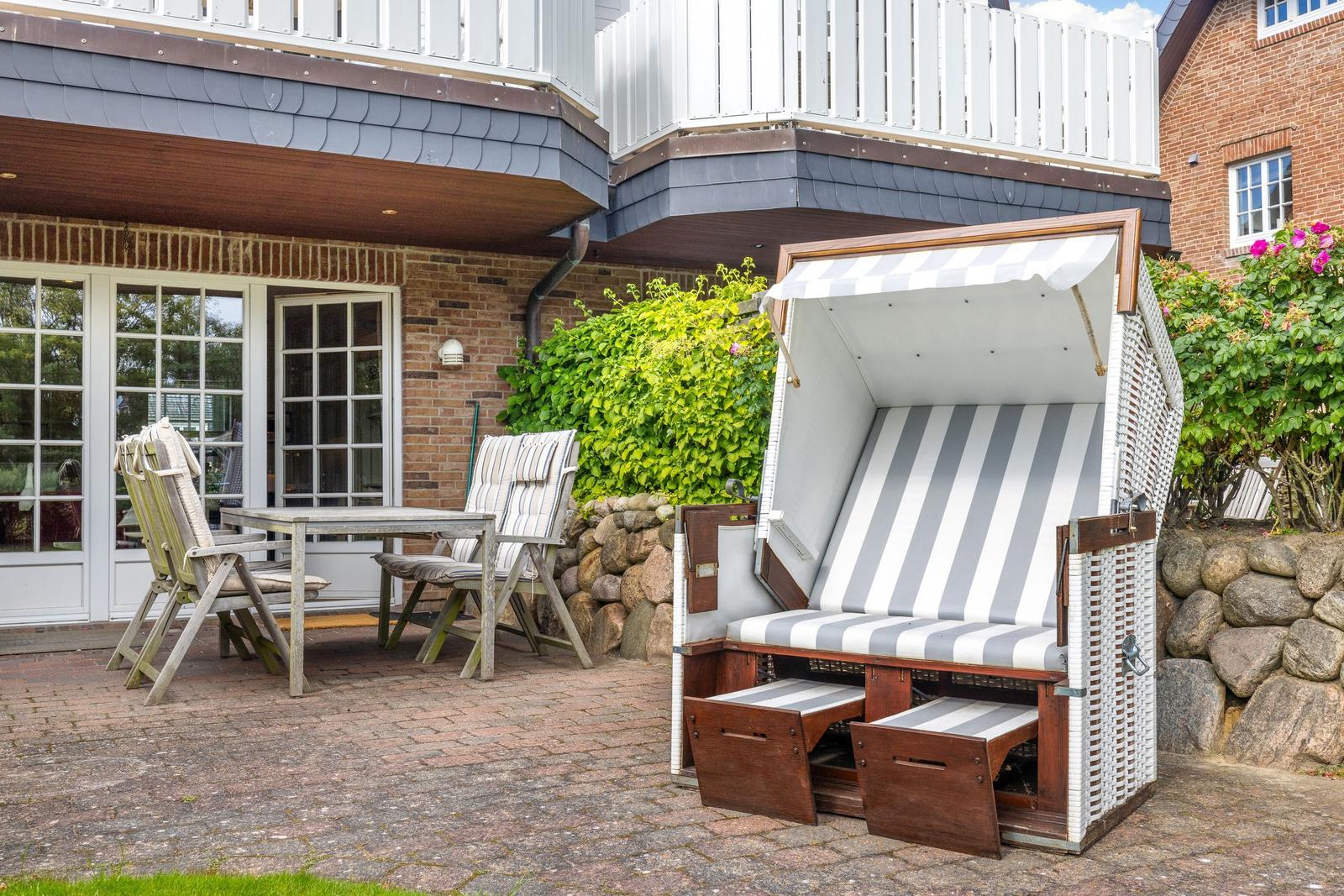 Terrasse mit Gartenliege, Tisch und Stühlen vor Haus mit Holzveranda.