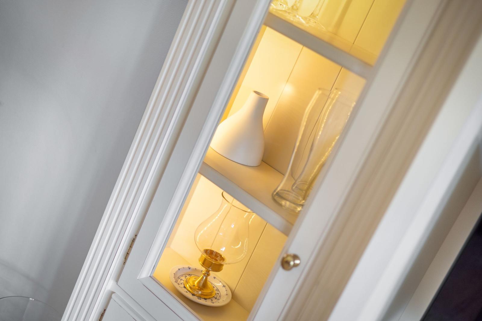 Weißer Schrank mit beleuchteten Regalen und Glasgegenständen.