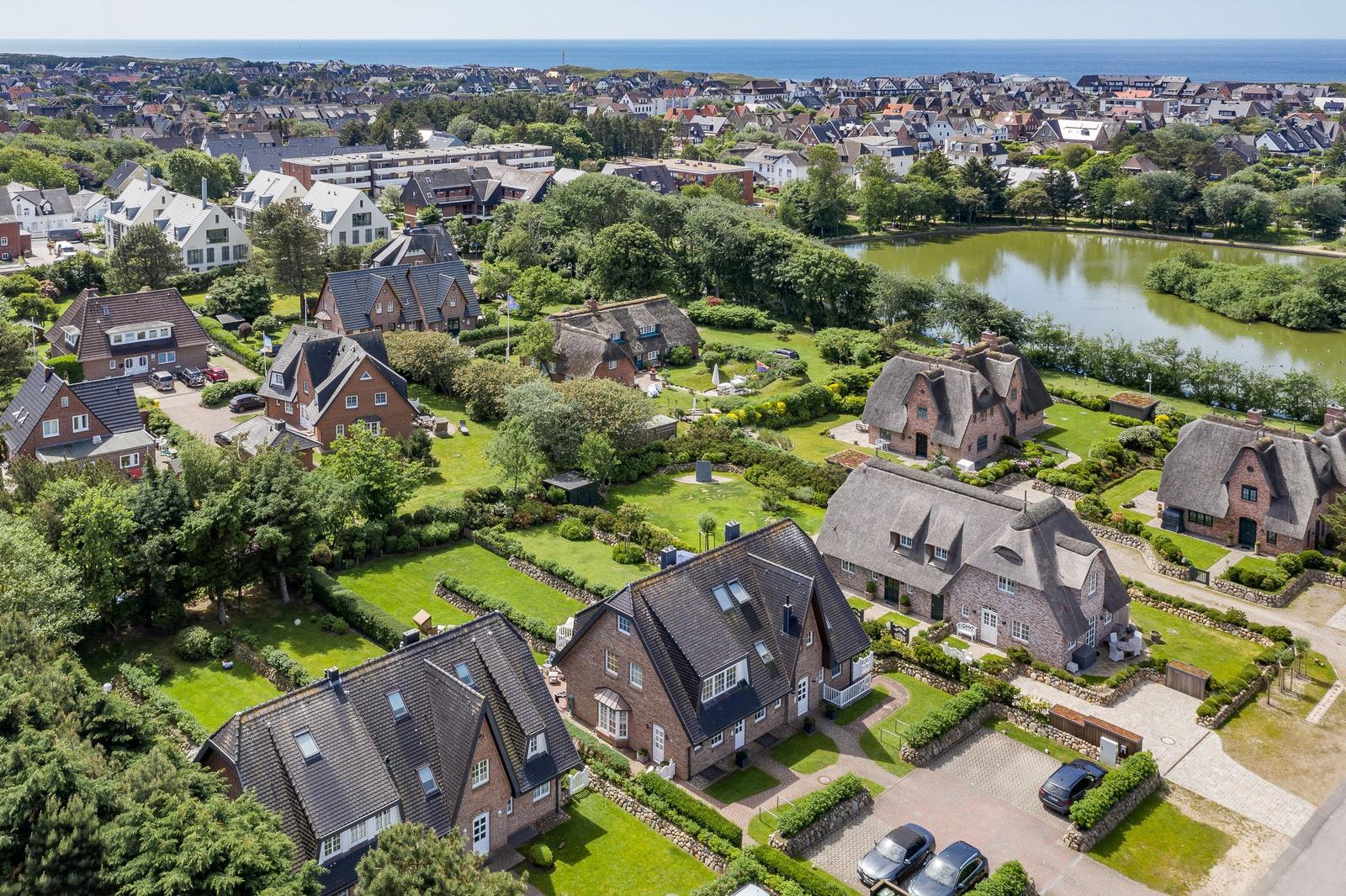 Luftbild von Häusern mit Grünflächen und einem See, im Hintergrund das Meer.