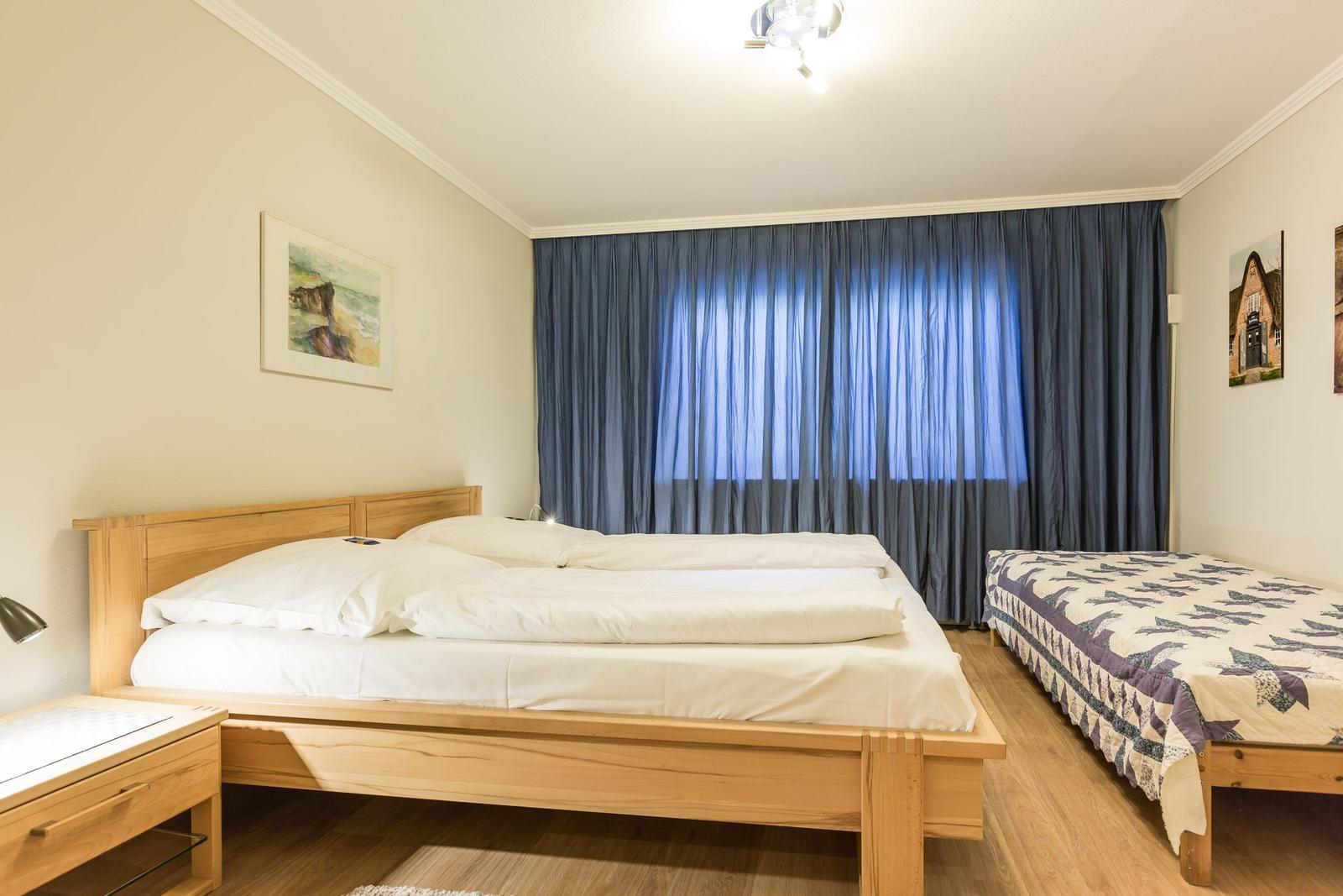 Zimmer mit Doppelbett und Einzelbett, blauen Vorhängen und Holzmöbeln.