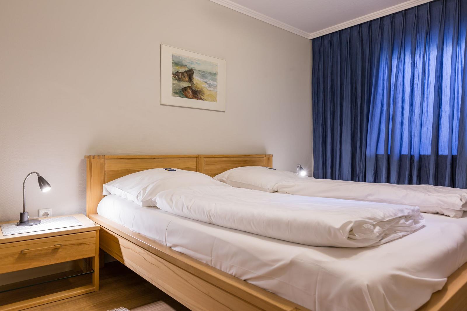Ein Schlafzimmer mit Holzbett, Nachttisch und blauen Vorhängen.
