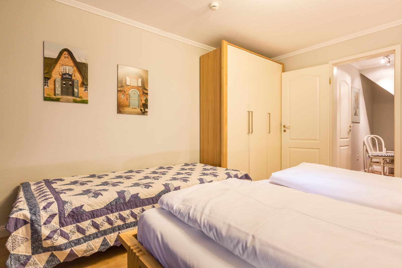 Zwei Betten, Kleiderschrank und Wandbilder in einem Schlafzimmer.